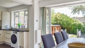 Een moderne keuken met een ingebouwde wasmachine, een eethoek met een tafel en stoelen, en uitzicht op de tuin door grote ramen.
