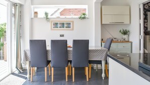 Een moderne eetruimte met een tafel en stoelen, een keuken met kastjes, en een raam met uitzicht op gebouwen.