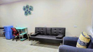 Ein Wohnzimmer mit einer Couch, einem kleinen Tisch, einem blauen Kühlschrank und einer Wanddekoration.