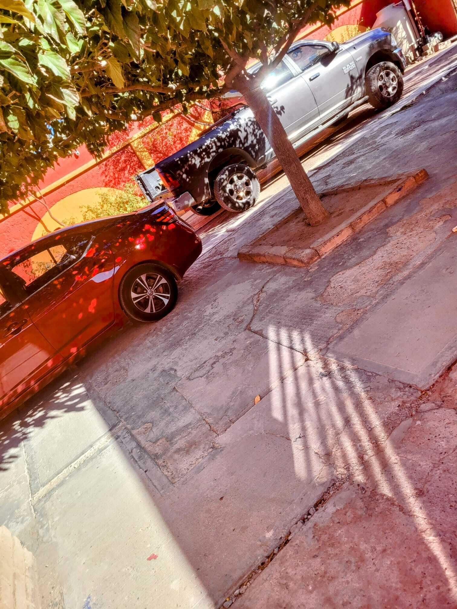 Un coche dañado en una calle con un árbol y un edificio al fondo.