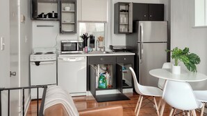 Cocina compacta con electrodomésticos blancos, comedor con sillas blancas y una planta en maceta.