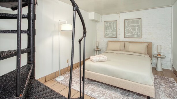 Un dormitorio con una cama, una escalera de caracol, una lámpara de pared y arte abstracto en la pared.