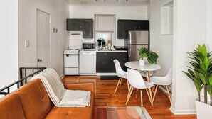 Una cocina compacta con electrodomésticos modernos, un comedor con sillas blancas y un sofá de cuero marrón.
