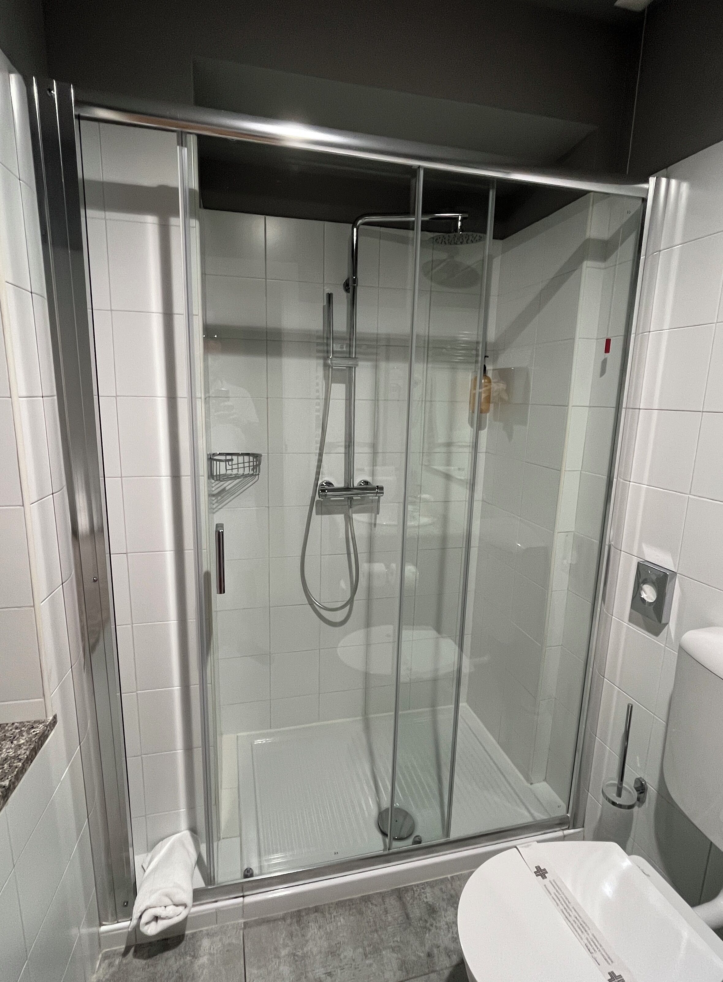 A modern bathroom with a glass-enclosed shower, a white toilet, and a granite countertop.