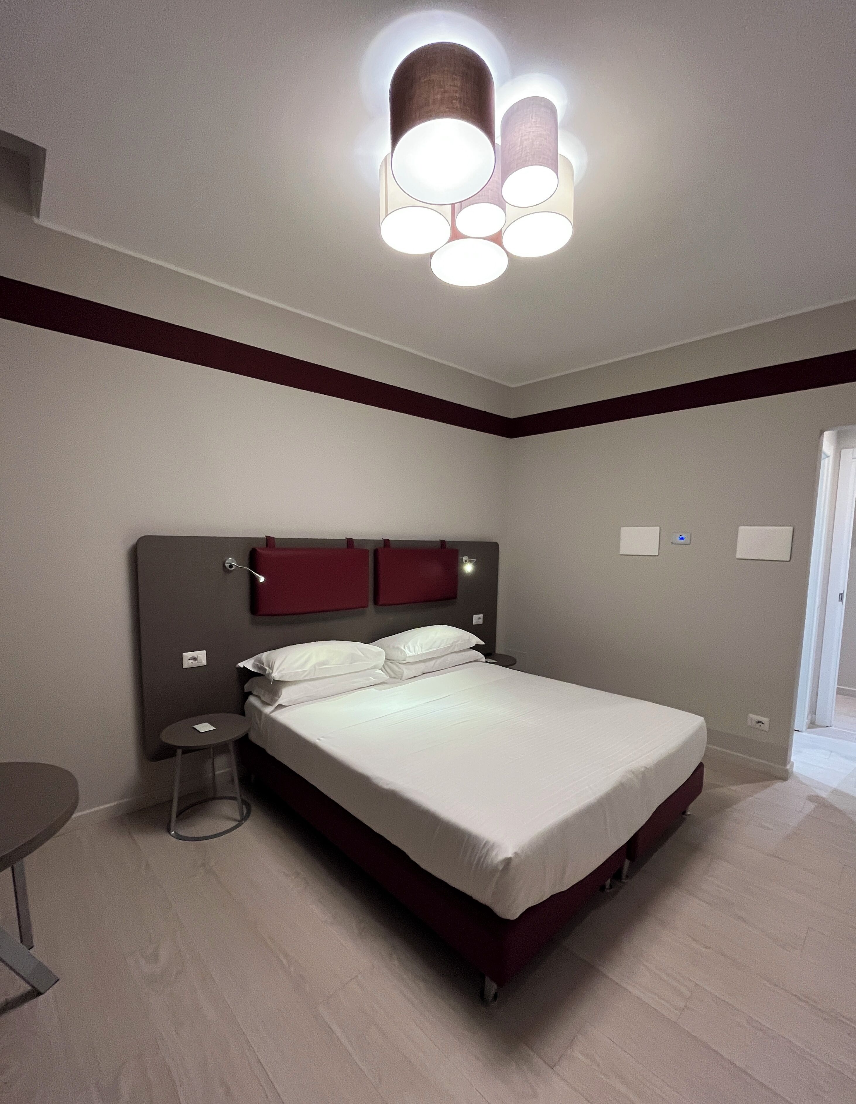 A modern hotel room with a large bed, a round side table, and a ceiling light fixture.