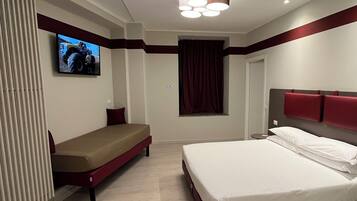 A hotel room with a bed, a sofa bed, a TV mounted on the wall, and a window with curtains.