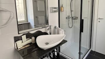 A modern bathroom with a black countertop sink, a large mirror, and a glass-enclosed shower.