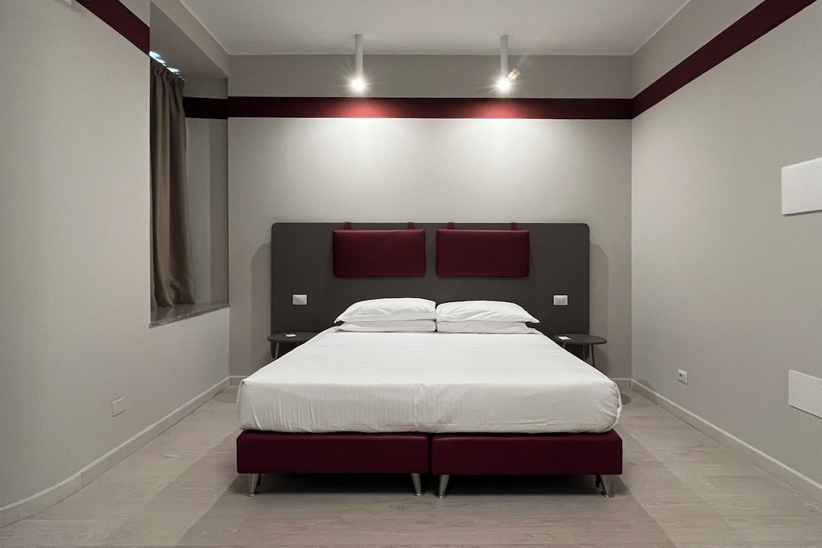 A modern bedroom with a large bed, two bedside tables, and a headboard with two red panels.
