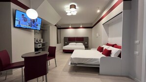 A modern hotel room with a bed, bedside tables, a TV, and a seating area with a chair and table. - Guest House Borgo Yporegia (Ivrea)