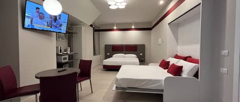 A modern hotel room with a bed, bedside tables, a TV, and a seating area with a chair and table.