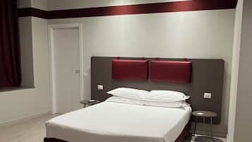 Quarto de hotel moderno com uma cama grande, duas mesas de cabeceira, uma parede de destaque vermelha e um lustre no teto.