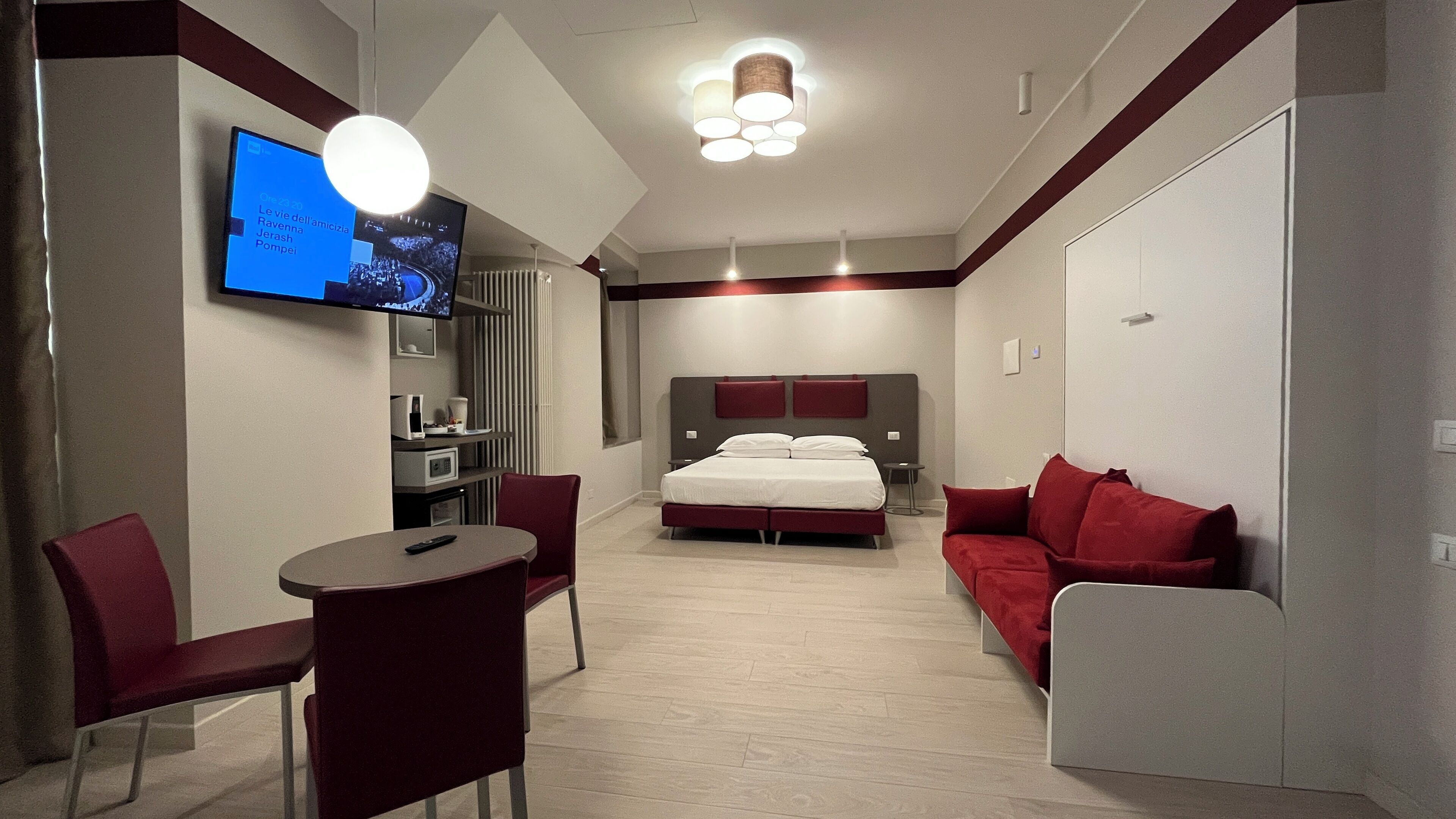 Una camera d'albergo con un letto, una TV, una scrivania e un divano rosso.