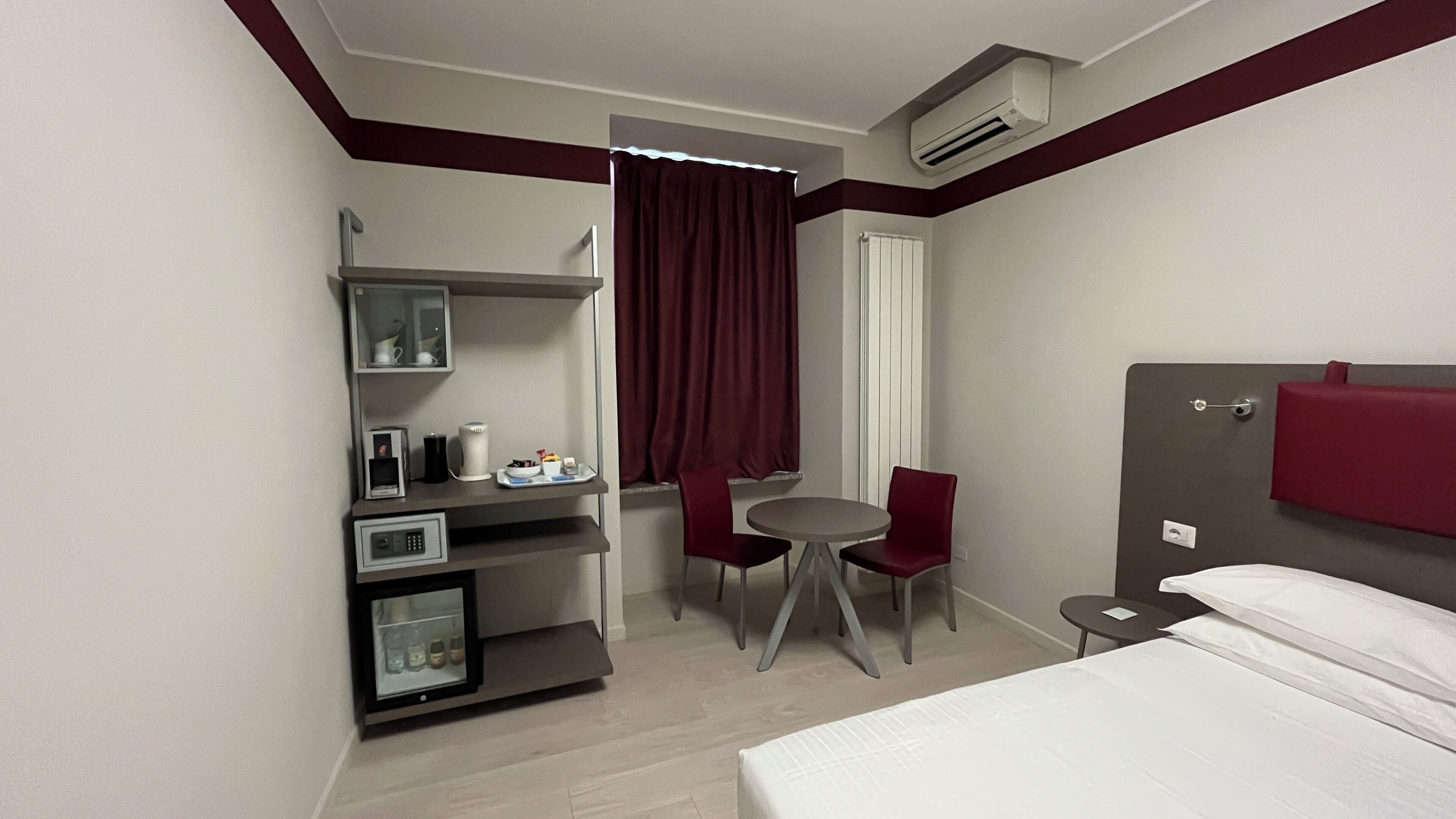 Ein Hotelzimmer mit einem Bett, einem Schreibtisch mit Computer, einem Stuhl, einem kleinen Tisch und einem Fenster mit Vorhängen.