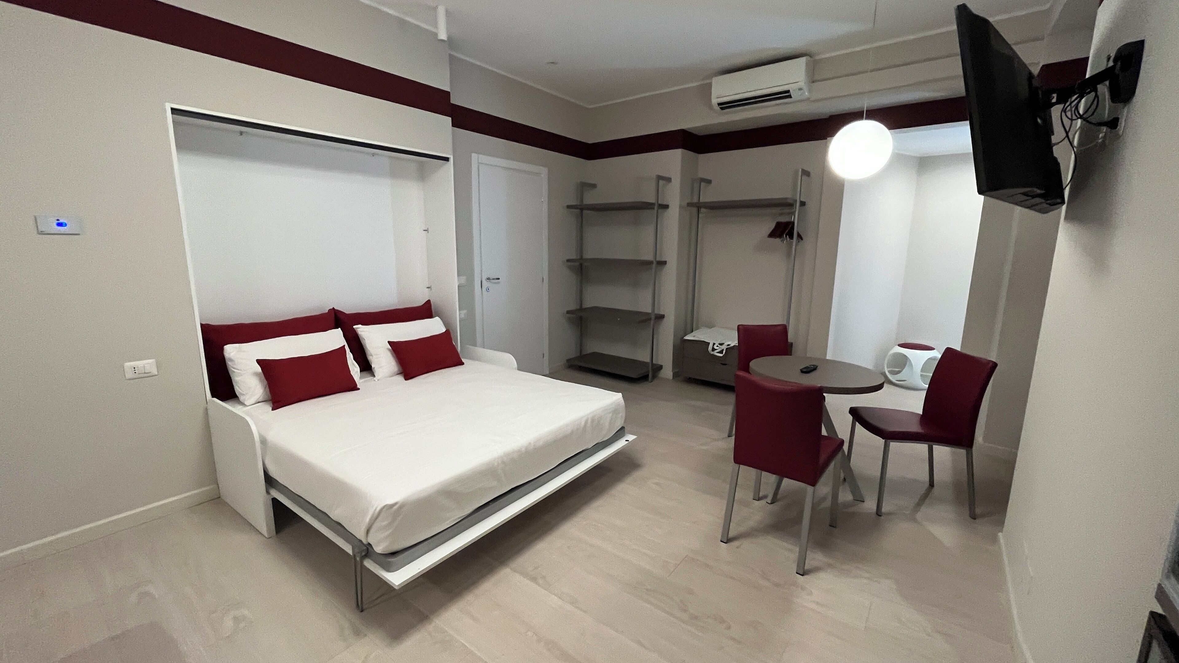 A hotel room with a bed, a desk, and a chair. There is a TV mounted on the wall.