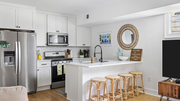 A modern kitchen with white cabinetry, stainless steel appliances, and a central island with bar stools. - A newly renovated classic Charleston home in the heart of downtown  (Charleston)
