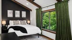 A bedroom with a large bed, a window with green curtains, and three wall-mounted paintings. - Cabin Near Banning State Park, the Munger Trail & Grindstone Lake -Dogs Welcome! (Sandstone)