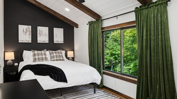 A bedroom with a large bed, a window with green curtains, and three wall-mounted paintings. - Cabin Near Banning State Park, the Munger Trail & Grindstone Lake -Dogs Welcome! (Sandstone)