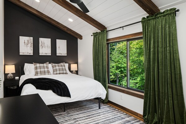A bedroom with a large bed, a window with green curtains, and three wall-mounted paintings. - Cabin Near Banning State Park, the Munger Trail & Grindstone Lake -Dogs Welcome! (Sandstone)