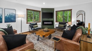 A modern living room with leather sofas, a coffee table, and large windows offering a forest view. - Cabin Near Banning State Park, the Munger Trail & Grindstone Lake -Dogs Welcome! (Sandstone)