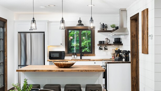 A modern kitchen with a central island, pendant lights, a large window with a forest view, and built-in appliances. - Cabin Near Banning State Park, the Munger Trail & Grindstone Lake -Dogs Welcome! (Sandstone)