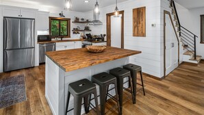 A modern kitchen with a wooden island, stainless steel appliances, and a staircase leading to another level. - Cabin Near Banning State Park, the Munger Trail & Grindstone Lake -Dogs Welcome! (Sandstone)