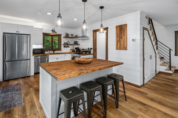 A modern kitchen with a wooden island, stainless steel appliances, and a staircase leading to another level. - Cabin Near Banning State Park, the Munger Trail & Grindstone Lake -Dogs Welcome! (Sandstone)