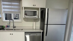 Una cucina moderna con mobili bianchi, lavastoviglie in acciaio inossidabile, frigorifero e forno a microonde.