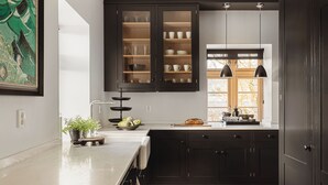 Una cocina con armarios oscuros, encimera de mármol y ventana con luz natural.