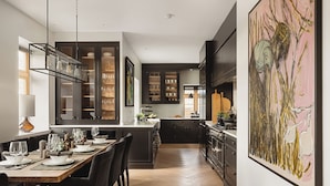Una cocina moderna con armarios oscuros, una mesa de comedor de madera dispuesta para seis personas y un cuadro abstracto grande en la pared.