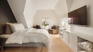Un dormitorio moderno con una cama, una silla, un televisor y una ventana.