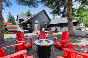 Un espace extérieur accueillant, aménagé avec des fauteuils Adirondack rouges disposés autour d’un foyer central, le tout adossé à un bâtiment en bois sombre doté d’un toit en pente.
