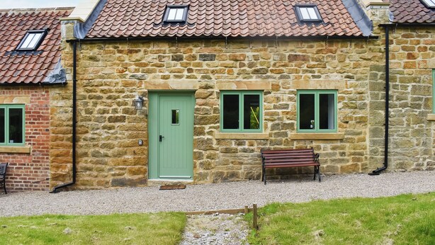 A stone building with a green door, two windows, and a bench. - UK47385 - The Deer Den (Easington, near Staithes)
