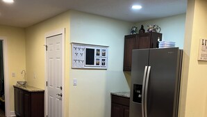 A kitchen with granite countertops, a stainless steel refrigerator, wooden cabinets, and recessed ceiling lights.