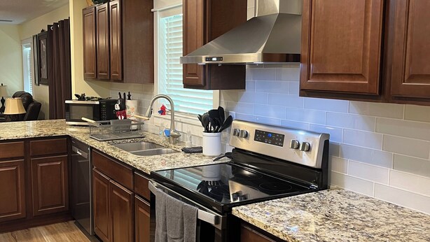 A modern kitchen with wooden cabinets, a stainless steel stove, and granite countertops.