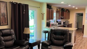 A spacious living room with leather chairs, a glass coffee table, and a ceiling fan.
