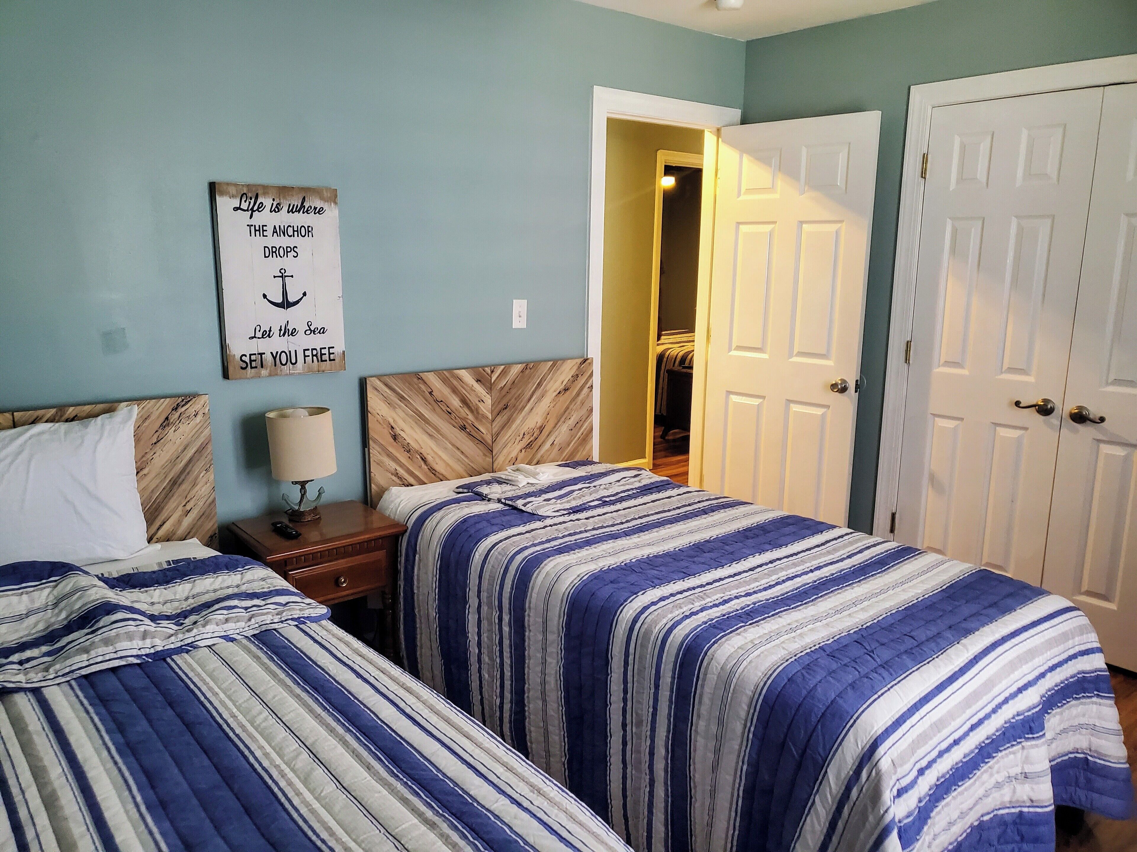 A bedroom with two beds, a nightstand, a lamp, and a motivational quote on the wall.