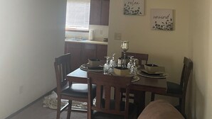 A dining area with a table set for four, surrounded by wooden chairs. There are two wall-mounted light fixtures above the table and a vent on the ceiling. - Beautiful little Magnolia in Las Cruses  (Las Cruces)