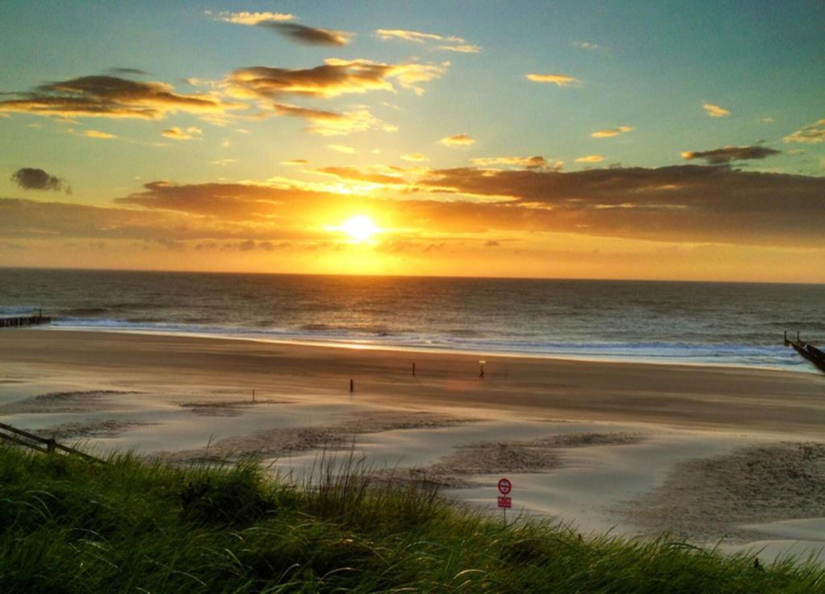 Une plage avec un coucher de soleil, une jetée et un panneau indiquant qu'il est interdit de se baigner.