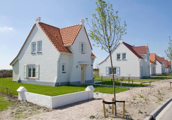 Une rangée de maisons blanches aux toits rouges, une pelouse verdoyante et un ciel dégagé.
