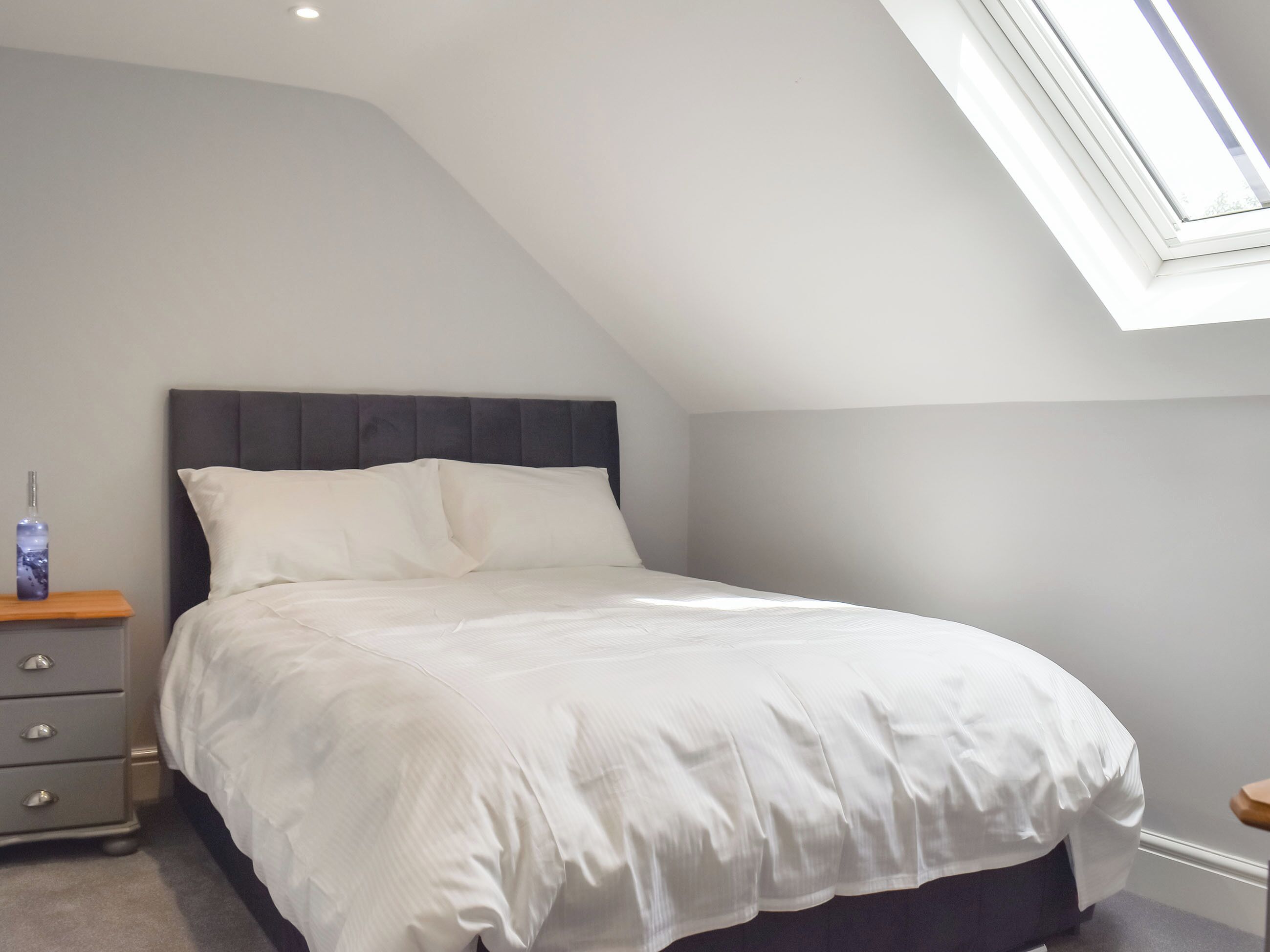 Une chambre à coucher comprenant un lit, une table de chevet, une commode et un puits de lumière.