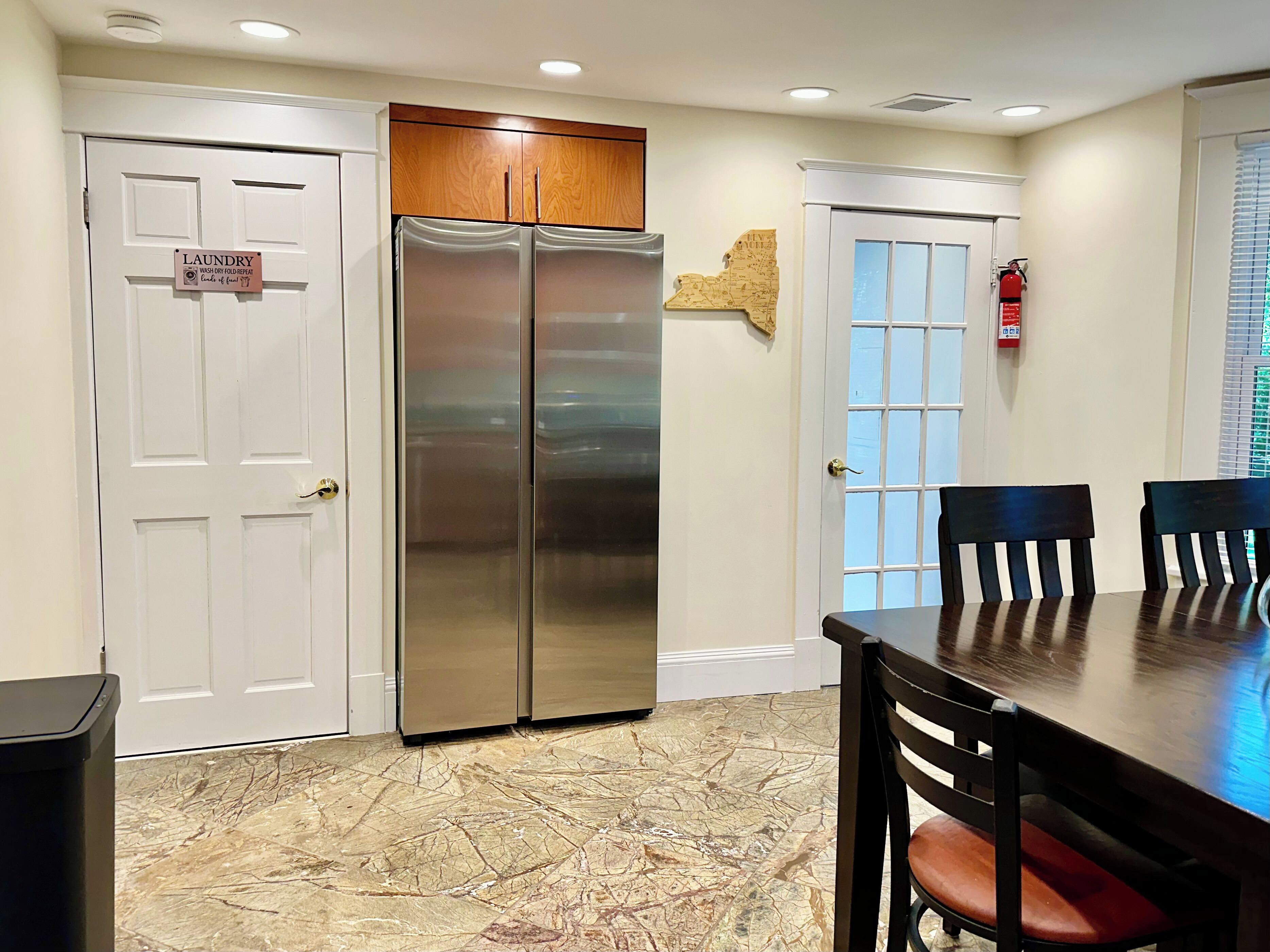 A kitchen with a stainless steel refrigerator, a dining table with chairs, and a map on the wall.