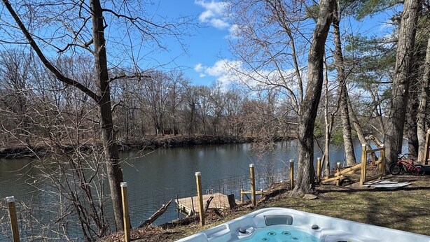 A hot tub by a lake with trees and a wooden fence.