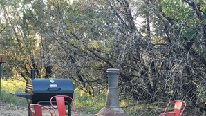 A barbecue grill, a metal chimney, and two red chairs in a gravel area with trees in the background. - Slow Your Roll - 2 King Suites • Near Bluff Dale Winery (Bluff Dale)