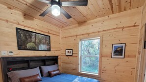 A wooden-paneled bedroom with a bed, ceiling fan, air conditioning unit, and a window. - Slow Your Roll - 2 King Suites • Near Bluff Dale Winery (Bluff Dale)