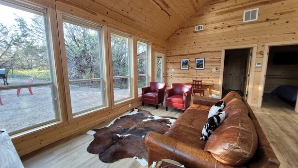 A log cabin interior with a leather sofa, red leather chairs, and a cowhide rug. - Slow Your Roll - 2 King Suites • Near Bluff Dale Winery (Bluff Dale)
