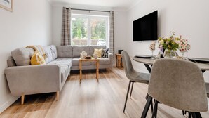 A modern living room with a grey sofa, a wooden coffee table, and a dining area with a table and chairs. - 2 bedroom accommodation in Lamlash (Lamlash)