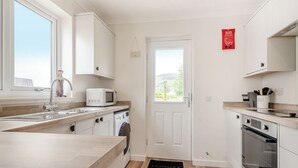 A modern kitchen with a built-in washing machine, a microwave, and a stove. - 2 bedroom accommodation in Lamlash (Lamlash)