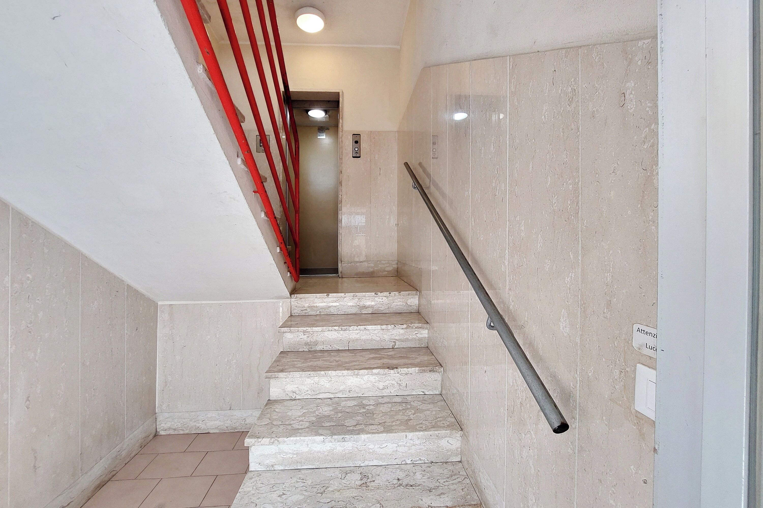 A marble staircase with a handrail, leading to an elevator.