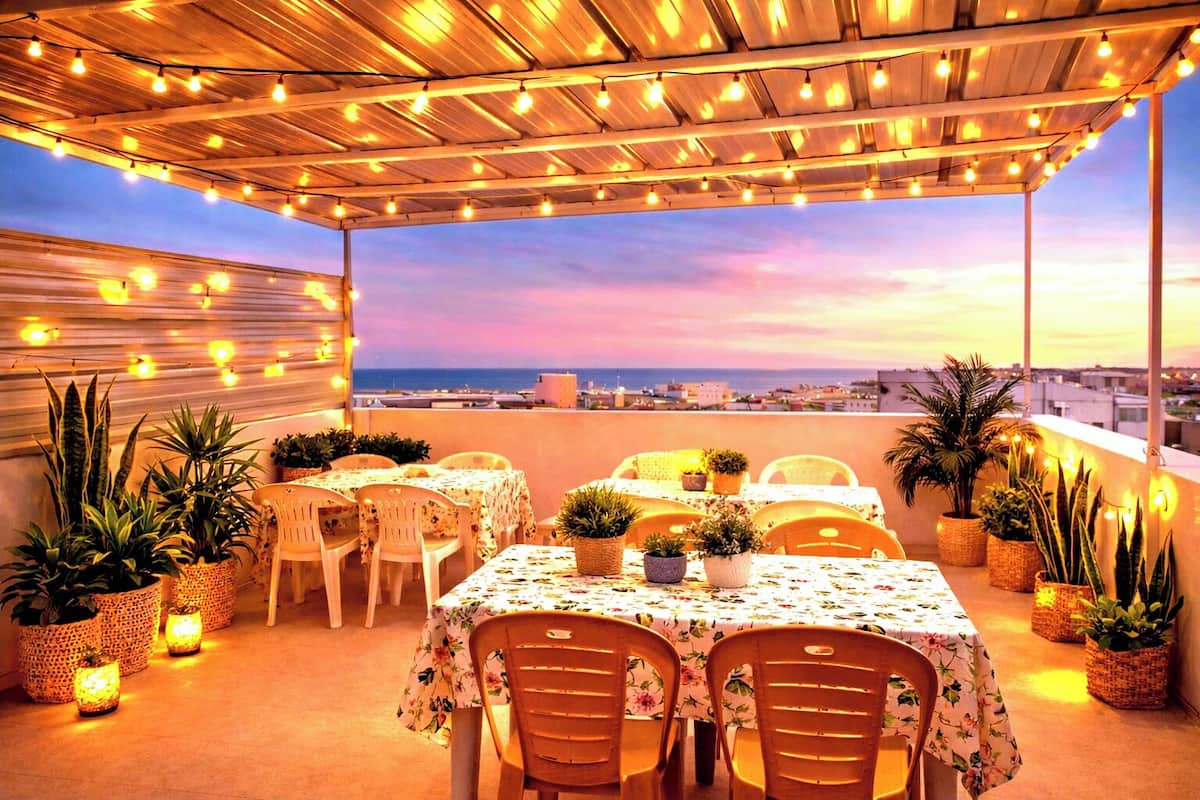 An outdoor dining area with tables and chairs, potted plants, and string lights.