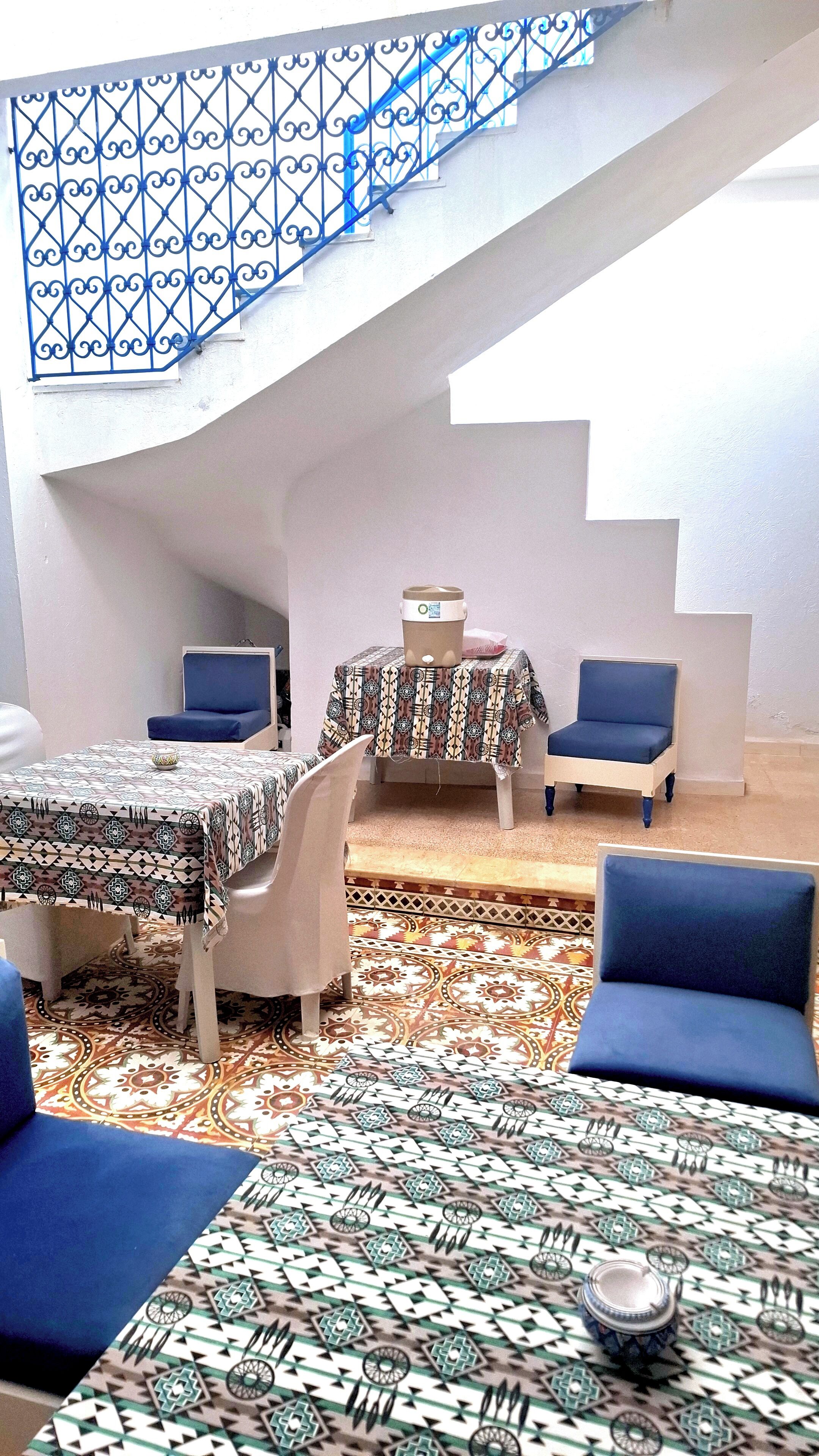A room with a staircase, a dining table with chairs, a sofa, and a patterned floor.